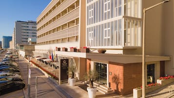 Un hotel moderno con varios balcones, un estacionamiento y vista a la calle.