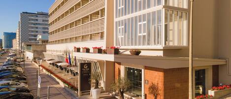 Un hotel moderno con varios balcones, un estacionamiento y vista a la calle.