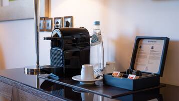 Estación de café en una habitación de hotel, con cafetera, botella de agua, tazas y un menú.