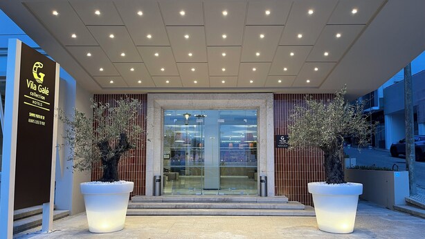 L’entrée d’un hôtel au design moderne, avec une porte en verre, des plantes en pot et un panneau indicateur.