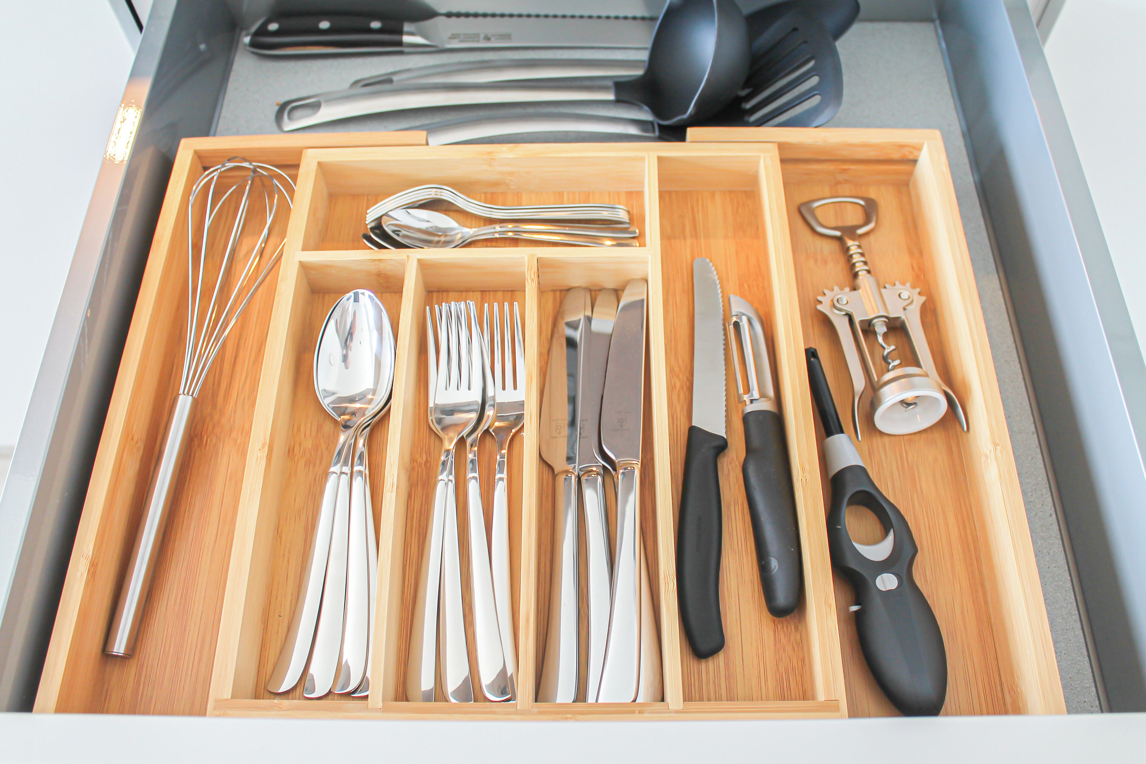 Un cassetto con utensili da cucina ordinatamente disposti, tra cui forchette, cucchiai, coltelli e cavatappi.