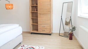 Ein Schlafzimmer mit Holzschrank, Spiegel, Nachttisch und Fenster.