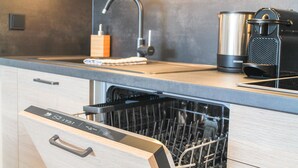 Eine moderne Küche mit Geschirrspüler, Edelstahl-Wasserkocher und Kaffeemaschine auf der Arbeitsfläche.