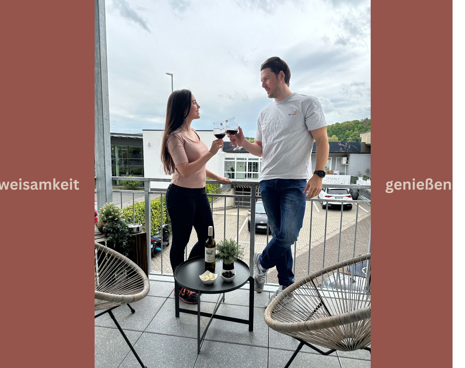 Um homem e uma mulher segurando copos de vinho em uma varanda com mesa, cadeiras e vista para um estacionamento.