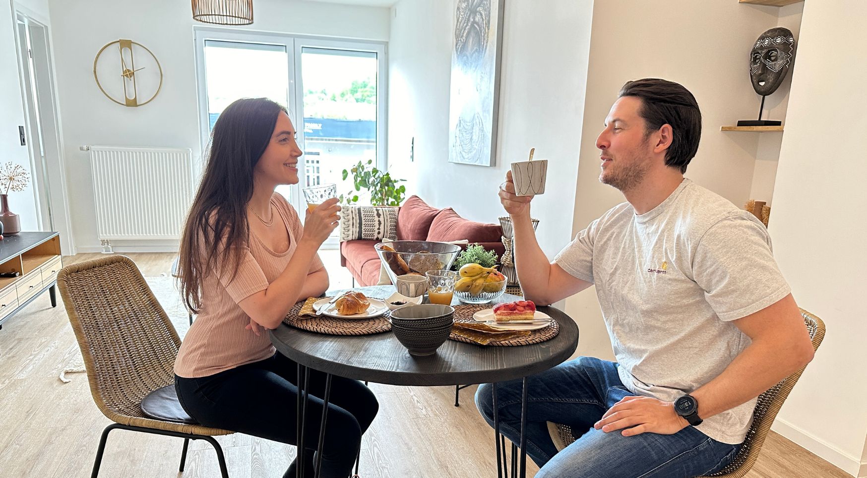 Zona pranzo con tavolo rotondo, sedie in vimini e diversi cibi.