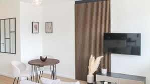 Ein modernes Wohnzimmer mit einer Couch, einem Esstisch, Stühlen, einem Fernseher und einer Wandverkleidung.