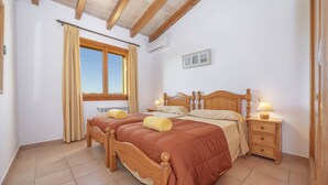 A bedroom with two wooden beds, a window with curtains, a bedside table with a lamp, and a wall-mounted air conditioner. - Els Evols for 6 with pool between Pollensa and Alcudia (Alcúdia)