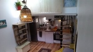 Een compacte woonruimte met een kitchenette, een eethoek en een zithoekje met een rode bank en kussens.