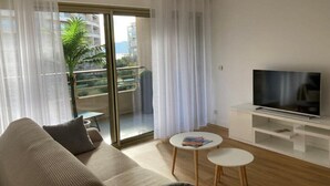 A modern living room with a sofa, two small tables, a TV, and a sliding glass door to a balcony. - Beautiful family cocoon of 65 m² close to the sea (Cannes)