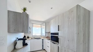 A modern kitchen with light wood cabinetry, a built-in oven, and a window providing natural light. - Pretty cocoon with harbour view (Porto-Vecchio)