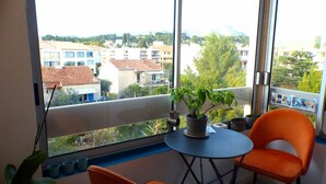 A balcony with a table and two chairs, a potted plant, and a view of buildings and greenery.