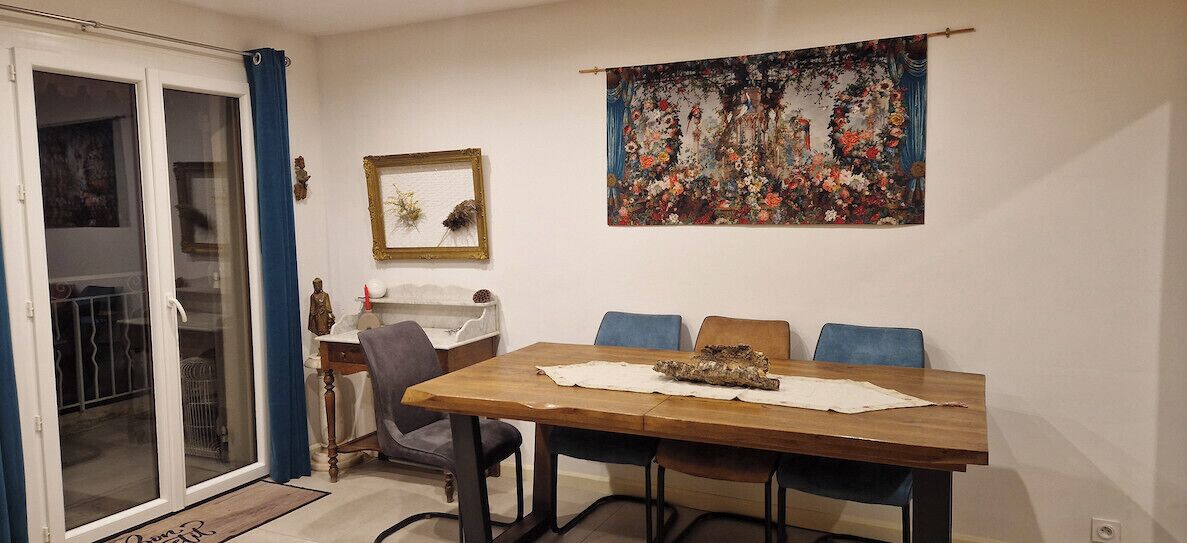 A dining area with a wooden table, blue chairs, a painting on the wall, and a sliding glass door.