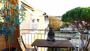 A balcony with a wooden table, two chairs, a potted plant, and a Buddha statue.