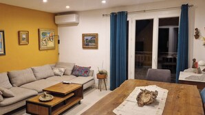 A living room with a sofa, coffee table, and a dining table. There are three framed pictures on the wall.