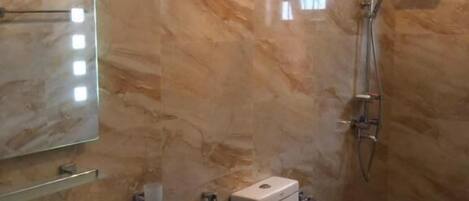 A bathroom with a marble wall, a sink, a toilet, and a shower.
