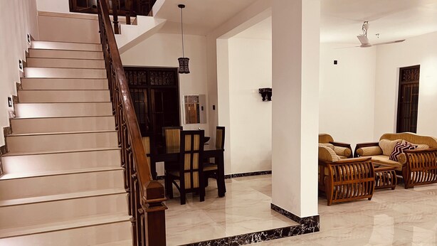 A spacious living area with a marble floor, a wooden staircase, and a seating area with sofas and chairs. - Ahasna Family Villa (Negombo)