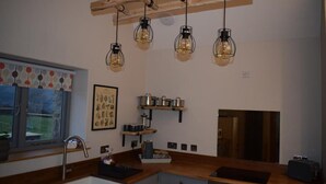Cocina moderna con encimera de madera, un lavaplatos integrado y lámparas colgantes. Hay estanterías con utensilios de cocina y una ventana con vistas.