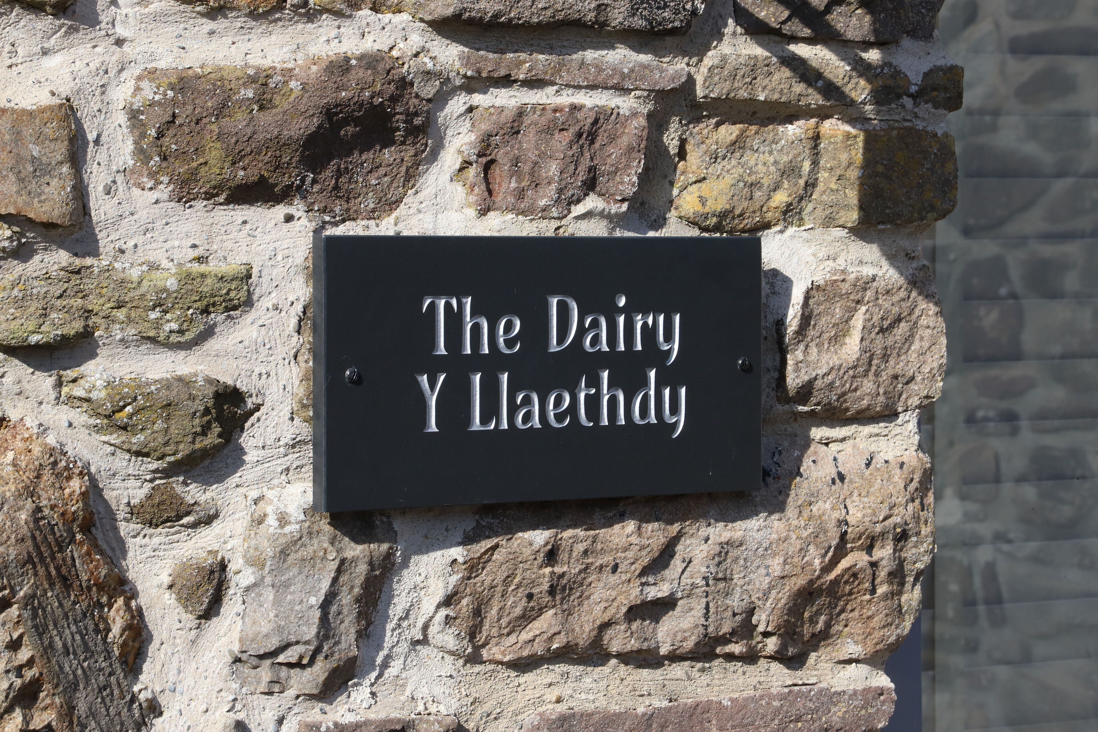 Een bord aan een stenen muur met de tekst 'The Dairy Y Llaethdy'.