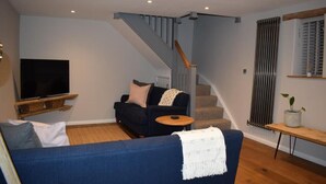 Una sala de estar con un sofá azul, un televisor sobre un mueble de madera, una escalera y un radiador.