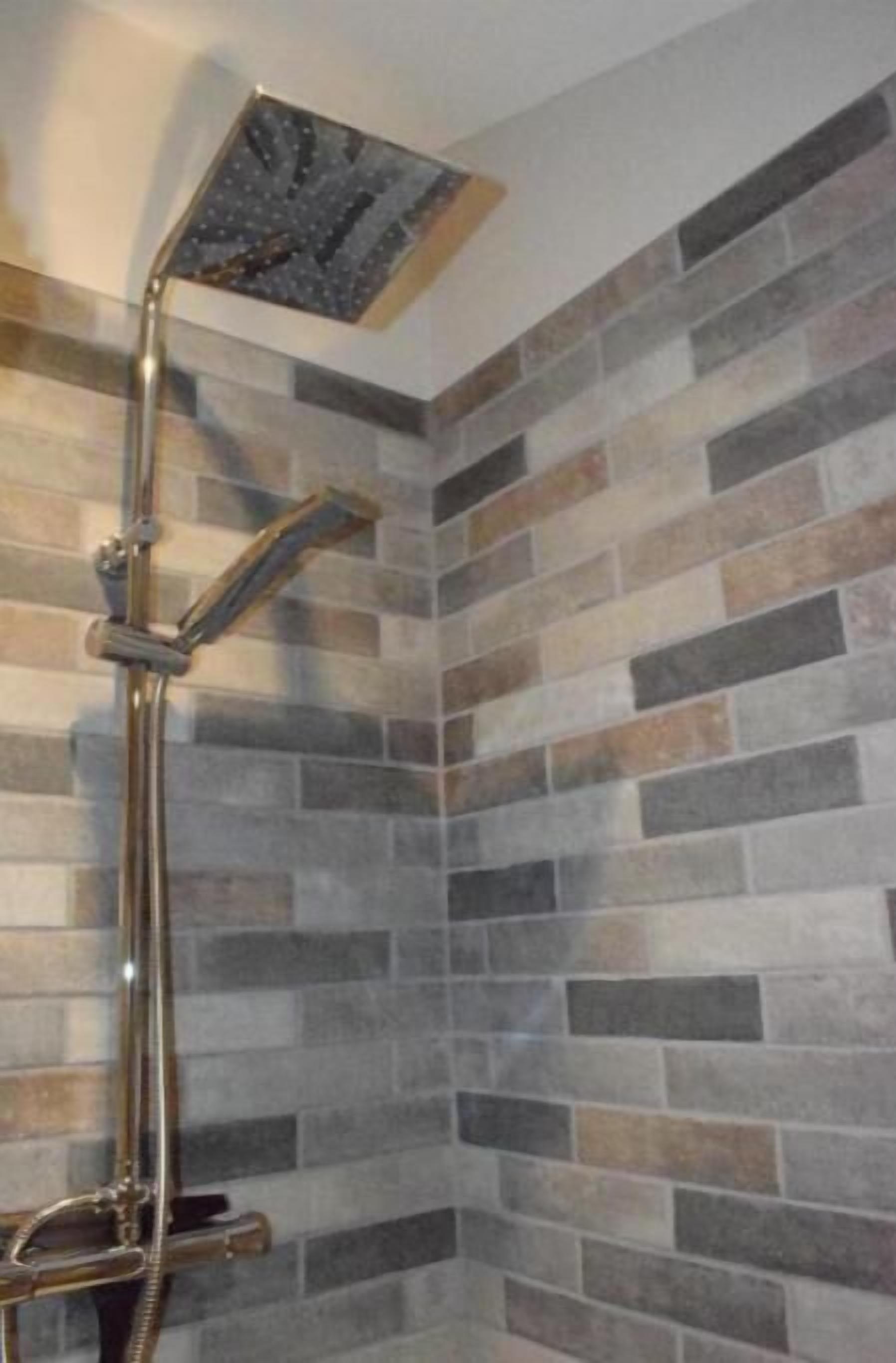 Une douche avec un pommeau carré et un flexible courbé.