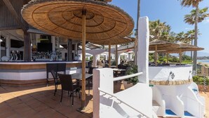 Un espace bar extérieur doté de parasols en chaume, de sièges et d’une zone piscine.