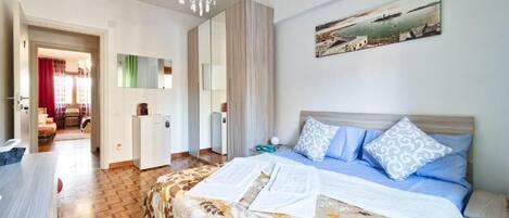 A bedroom with a bed, a desk, a chair, a wardrobe, and a painting on the wall.