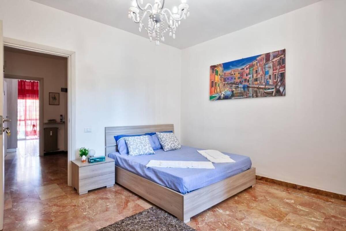 Un dormitorio con cama, mesita de noche, candelabro, cuadro y cortina roja.