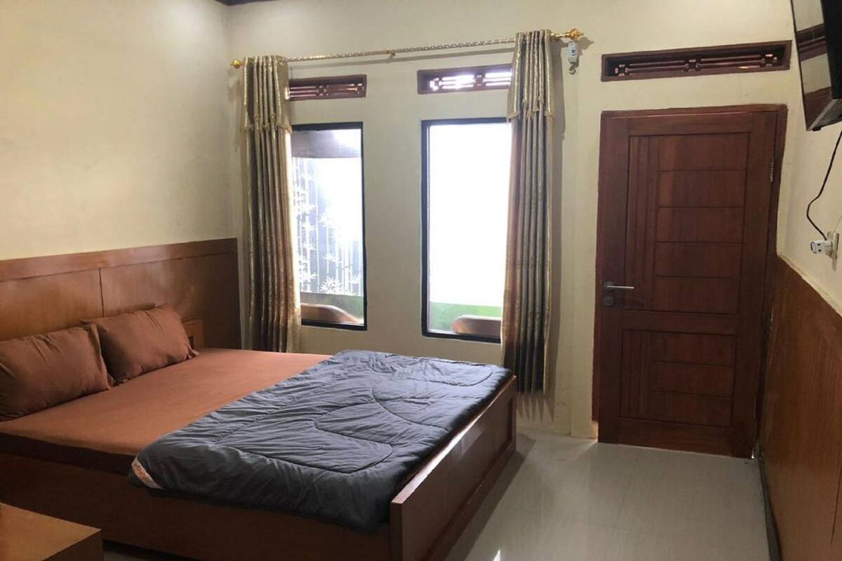 Une chambre à coucher avec un lit, une porte en bois et deux fenêtres avec des rideaux.