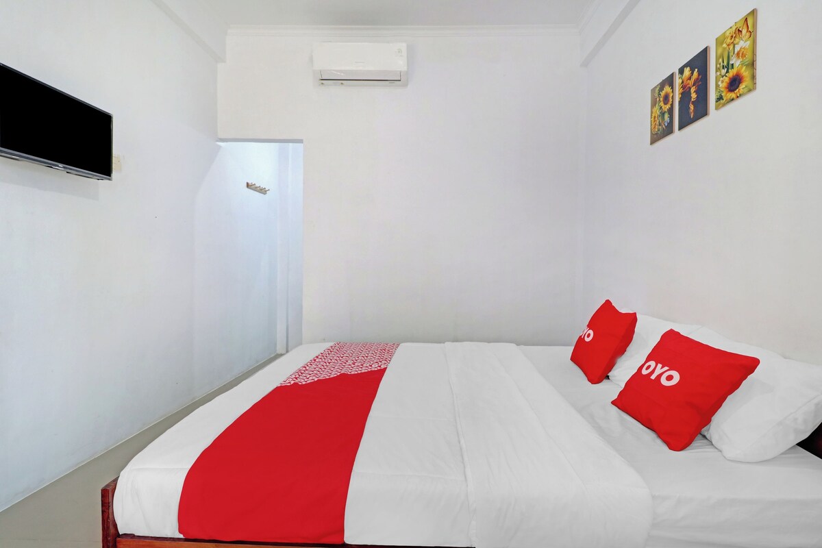 A hotel room with a bed, a TV, an air conditioner, and a door.
