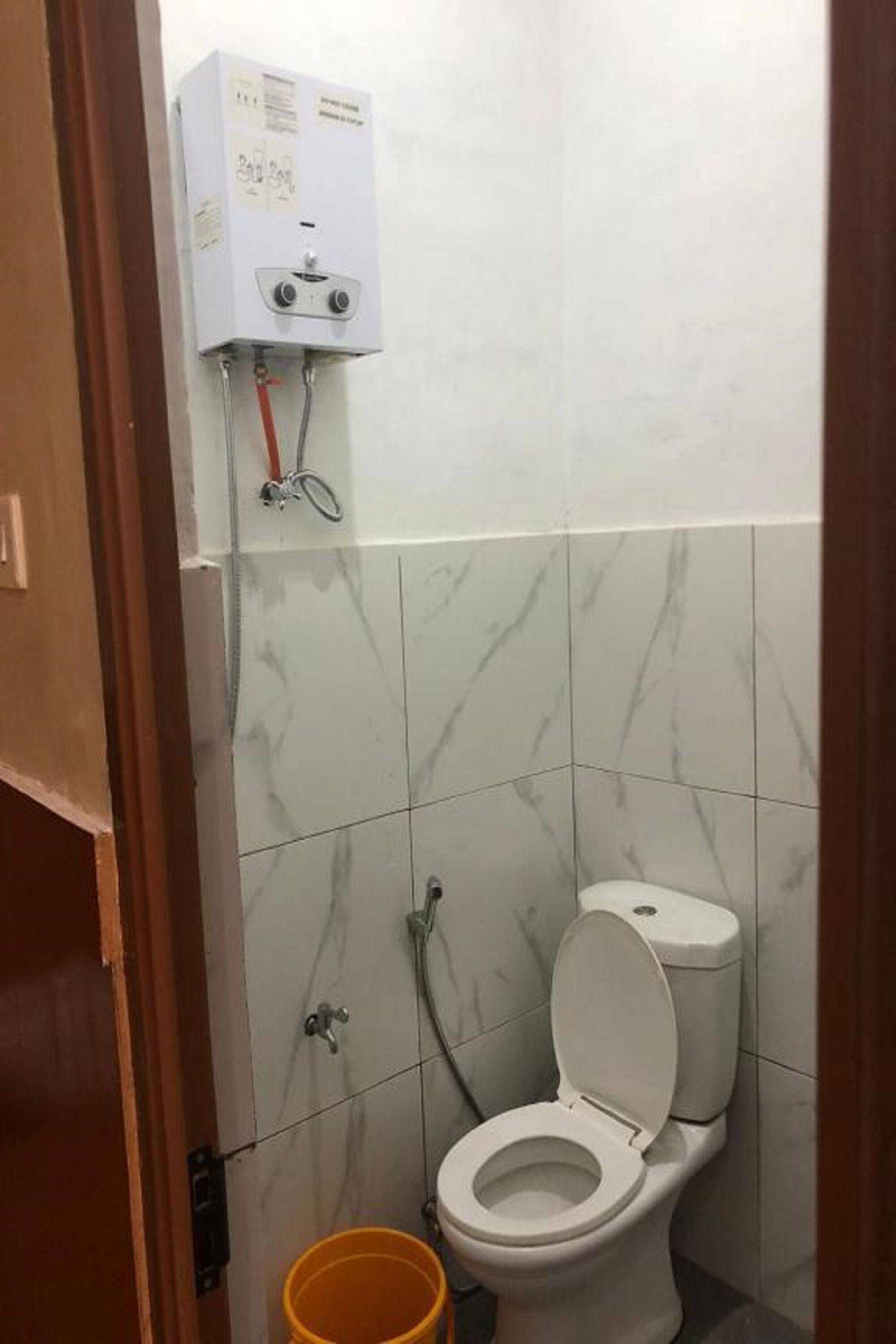 A bathroom with a toilet, a water heater, and a yellow bucket.