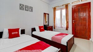 A hotel room with two beds, each with red and white bedding, a wooden door, and a window with curtains. - OYO Life 90570 Heboh Guest House Syariah (Majalaya)