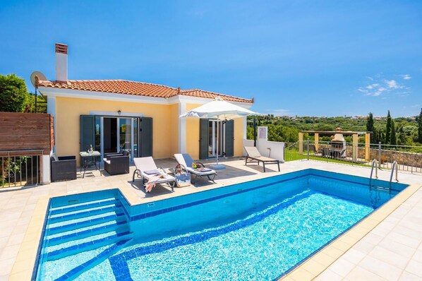 Una piscina amb gandules i ombrel·les, un porxo cobert i vistes al camp.
