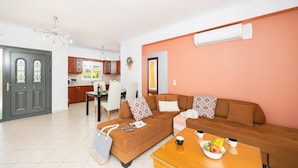 A modern living room with a brown sofa, a wooden coffee table, and a dining area with a kitchen in the background. - Europe Villa Io - Two Bedroom Villa, Sleeps 4 (Ionian Islands)
