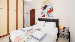 A neatly made bed with pillows and folded towels, a bedside table with a lamp, a wardrobe, and a painting on the wall. - Europe Villa Io - Two Bedroom Villa, Sleeps 4 (Ionian Islands)