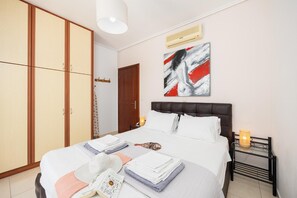 Una cama bien hecha con almohadas y toallas dobladas, una mesita de noche con lámpara, un armario y un cuadro en la pared.