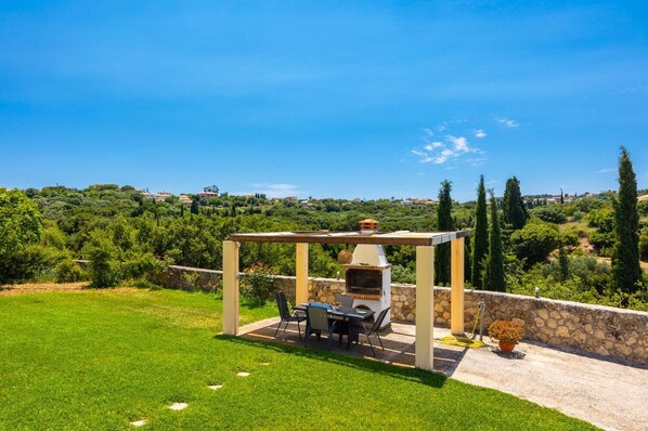Eine Terrasse mit Grill, Stühlen und Blick auf ein Weinberg und Hügel.