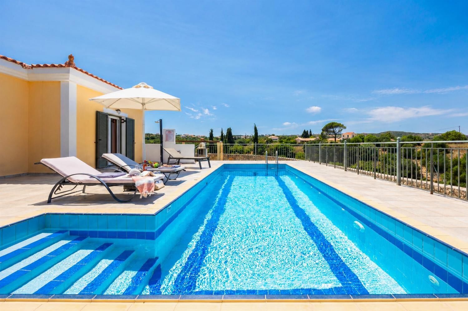 Une piscine rectangulaire à l’eau d’un bleu limpide, entourée d’une terrasse carrelée. On y trouve des chaises longues et un parasol.