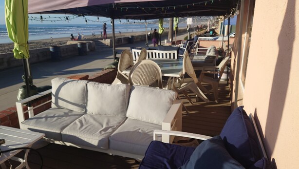 Une terrasse au bord de la plage, avec un canapé blanc, des fauteuils en osier et une table.
