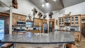 A spacious kitchen with a large island, wooden cabinets, and various decorative items including animal heads. - South Texas Ranch Getaway (Goliad)