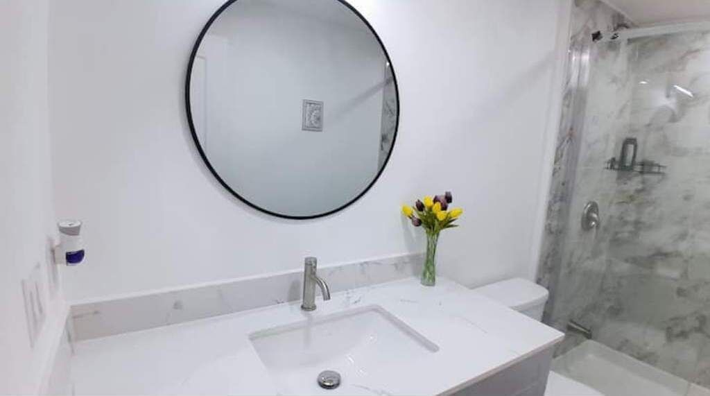 Une salle de bain avec un miroir rond, un lavabo et une douche.