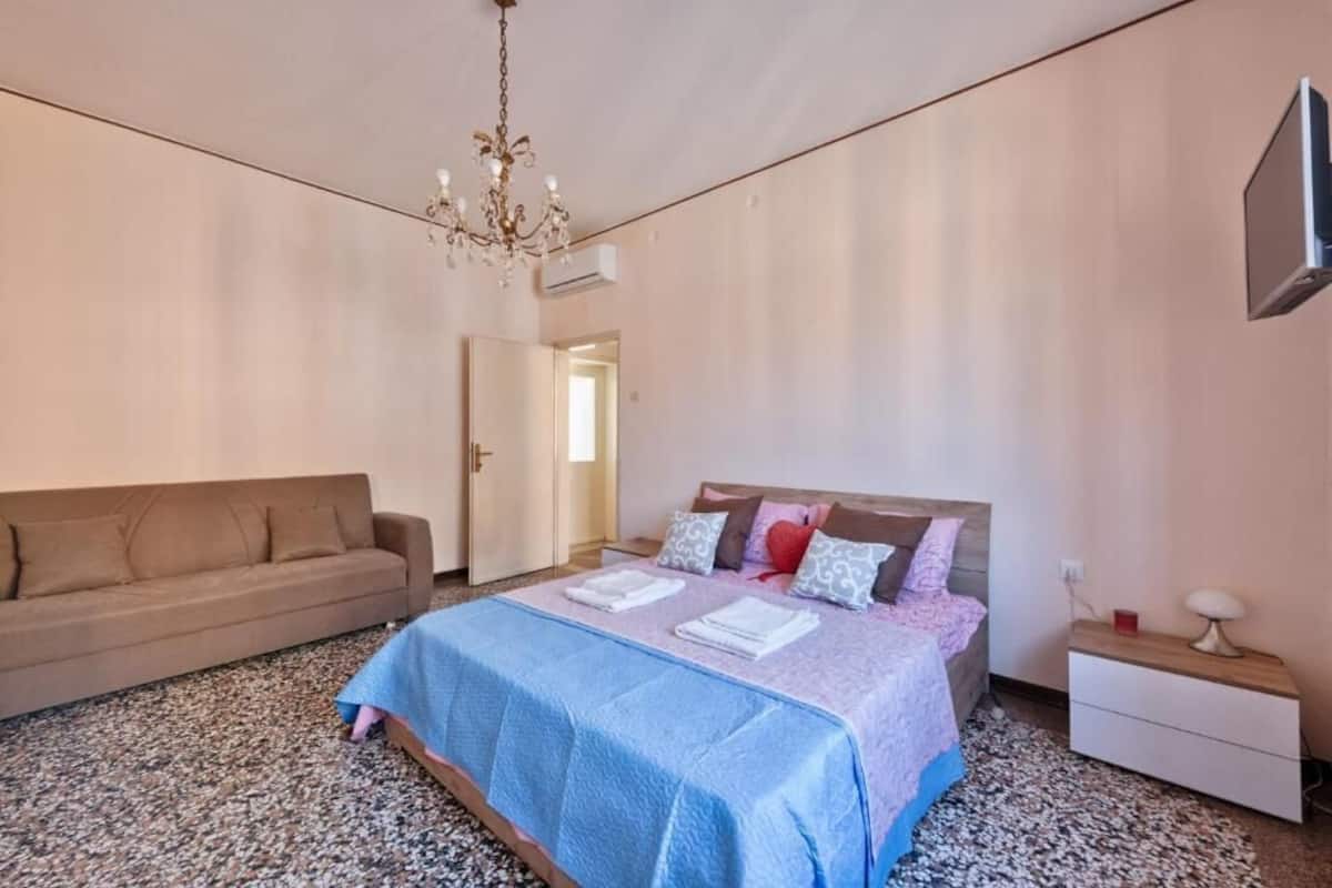 Un dormitori amb llit, sofà, tauleta de nit i televisió.