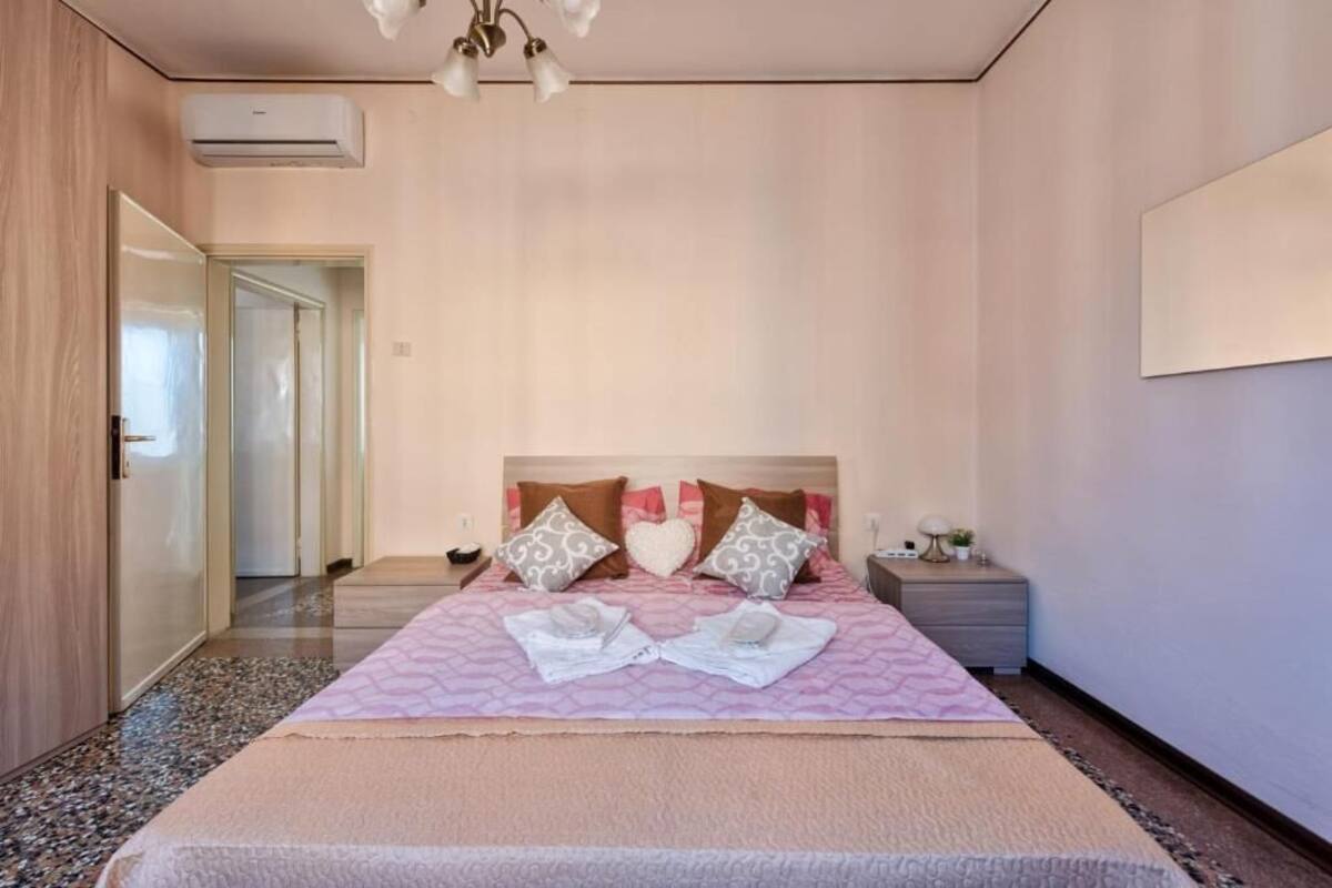 Un dormitori amb un llit, taules de nit, aire condicionat fixat a la paret i una porta que dona a una altra habitació.