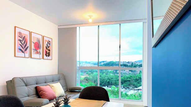 A modern living room with a grey sofa, a dining table with a placemat, and a large window offering a city view. - Wonderful apartment near the airport (Pereira)