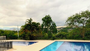 A rectangular swimming pool with clear blue water, surrounded by a tiled deck and a black metal fence. - Wonderful apartment near the airport (Pereira)