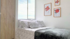 A bedroom with a bed, a wardrobe, a window, and three framed floral artworks on the wall. - Wonderful apartment near the airport (Pereira)