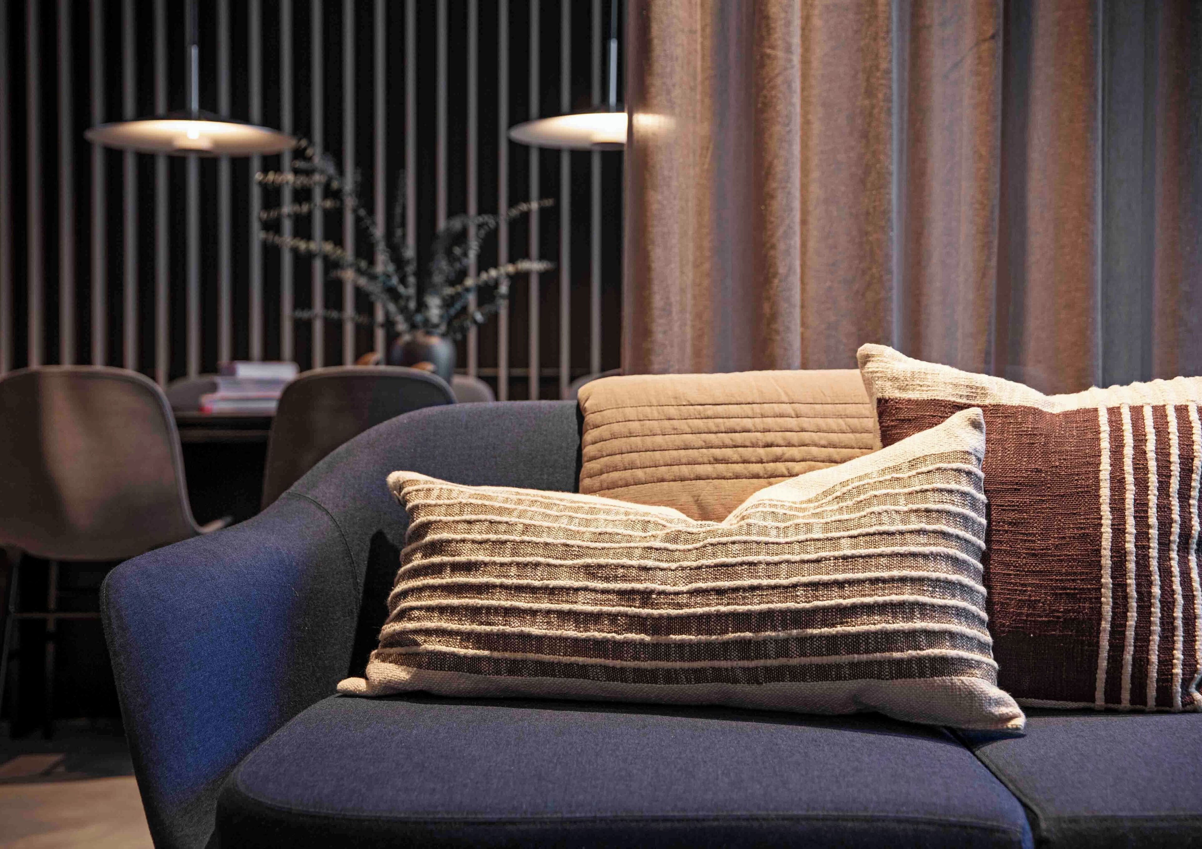 Una sala moderna con un sofá azul oscuro, dos almohadones con textura, y en el fondo, un comedor con mesa y sillas.