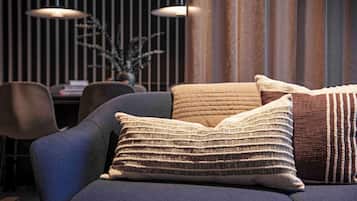 Una sala moderna con un sofá azul oscuro, dos almohadones con textura, y en el fondo, un comedor con mesa y sillas.