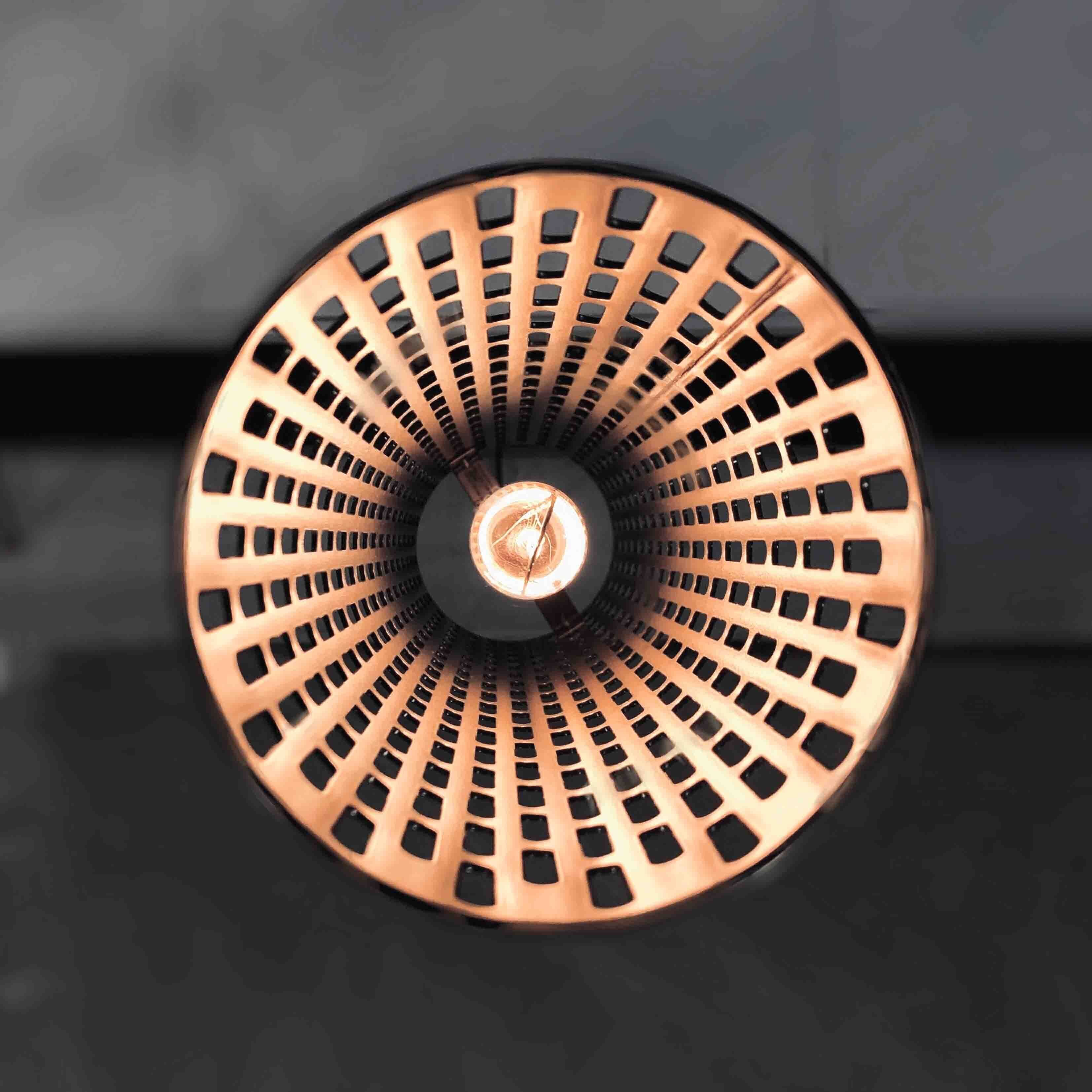 A circular copper object with a central hole and a pattern of evenly spaced holes around its circumference.