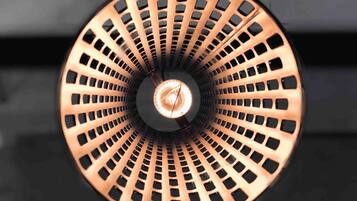 A circular copper object with a central hole and a pattern of evenly spaced holes around its circumference.