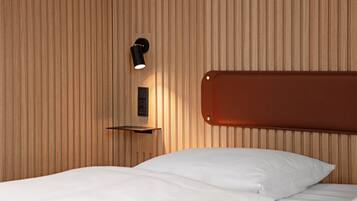 A hotel room with a wooden panel wall, a bed with white bedding, a mounted shelf, and a wall-mounted light fixture.